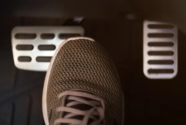 A person's sneaker pressing the brake pedal inside a car's dimly lit footwell, with the accelerator pedal visible to the right.