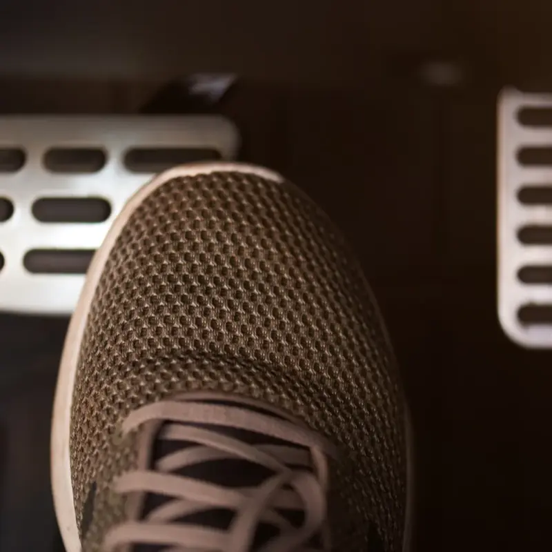 A person's sneaker pressing the brake pedal inside a car's dimly lit footwell, with the accelerator pedal visible to the right.