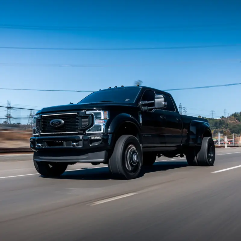 A black Ford F-450 dually pickup truck driving down a road on a clear sunny day with the background blurred by motion.